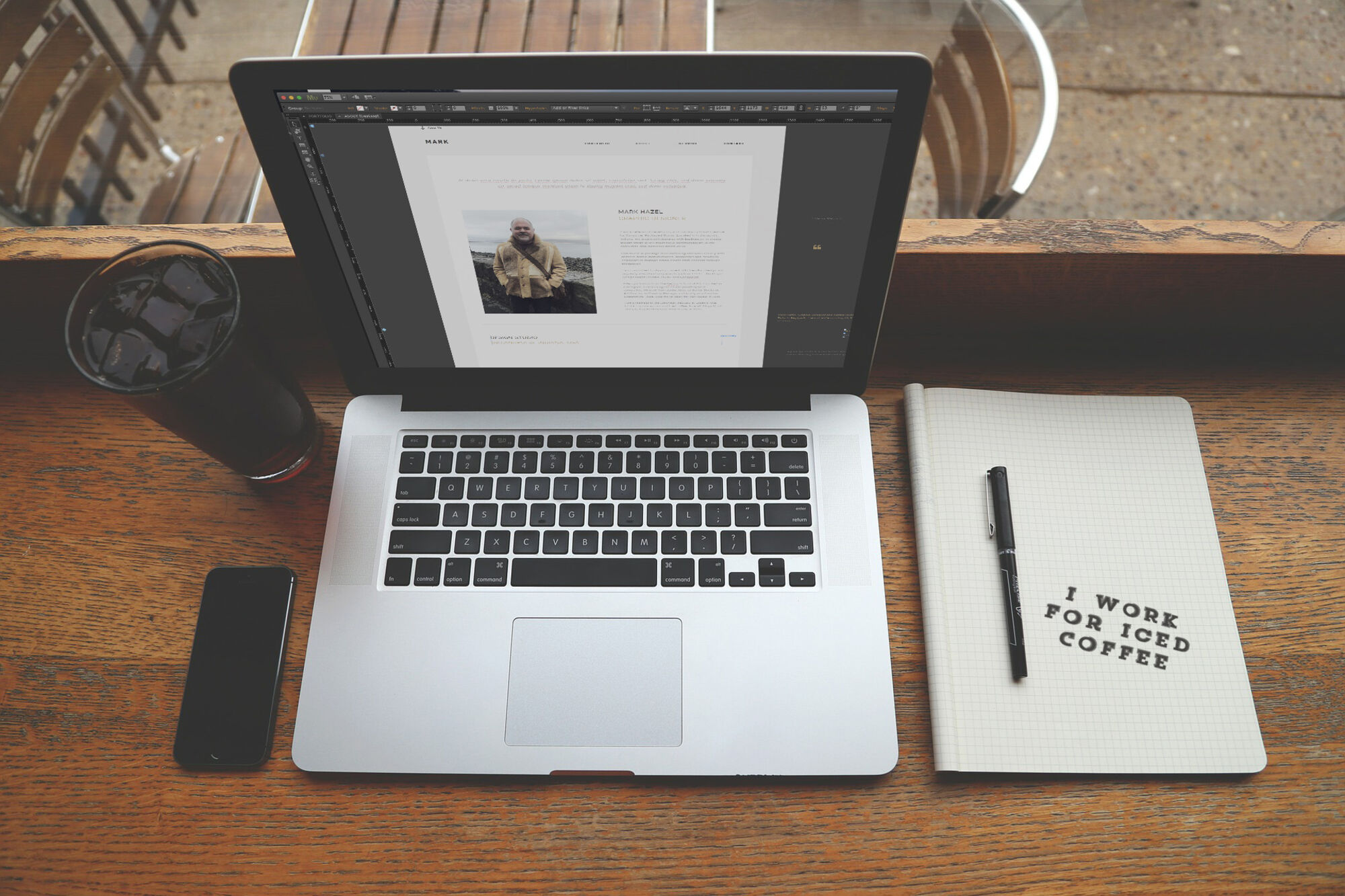 Designing on a laptop, with an iced coffee and a notebook that reads I work for iced coffee